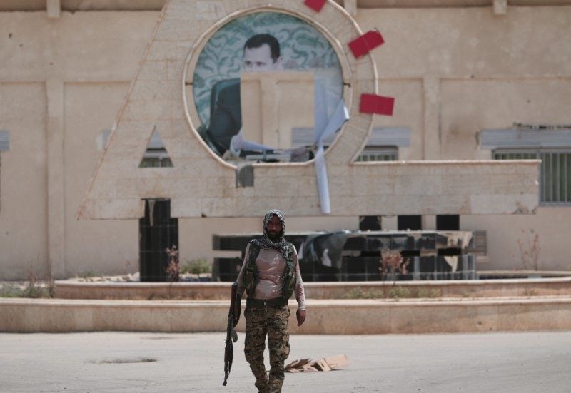 A Kurdish fighter from the People's Protection Units (YPG) carries his weapon as he walks at the faculty of economics where a defaced picture of Syrian President Bashar al-Assad is seen in the background, in the Ghwairan neighborhood of Hasaka, Syria, August 22, 2016. REUTERS/Rodi Said 