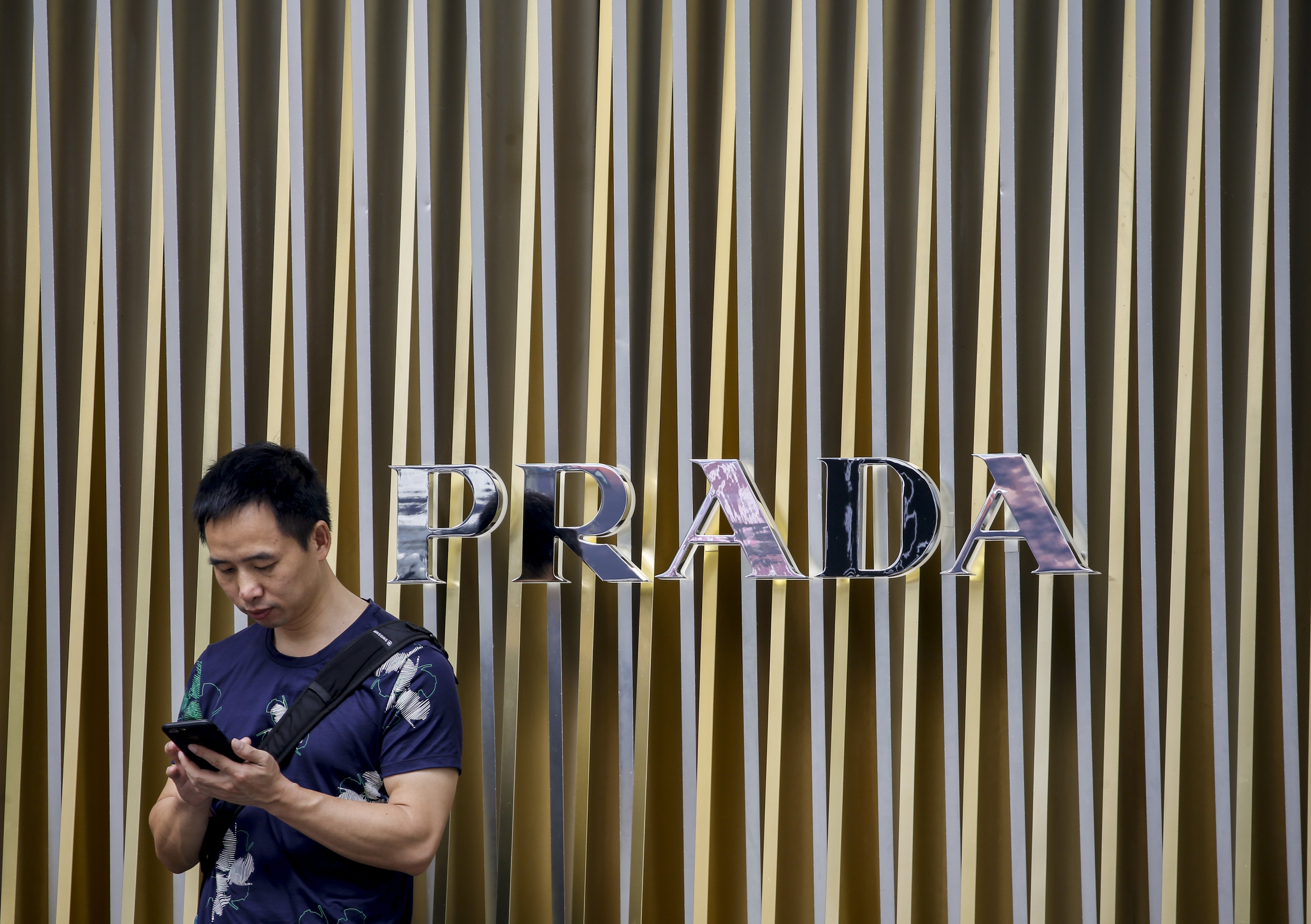 2017-07-14 10:19:38 epa06086327 A man looks at his phone while standing next to a Prada logo in Singapore, 14 July 2017. EPA/WALLACE WOON