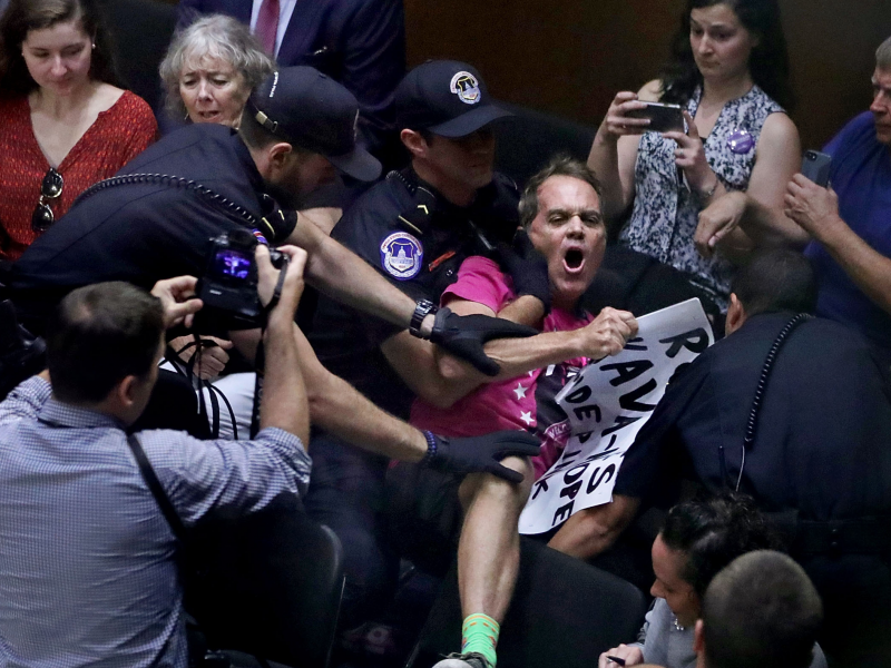 WASHINGTON, DC - SEPTEMBER 06: Code Pink demonstrator Tighe Barry is pulled down from a chair by a U.S. Capitol Police officer after he interrupted the third day of Supreme Court nominee Judge Brett Kavanaugh's confirmation hearing in the Hart Senate Office Building on Capitol Hill September 6, 2018 in Washington, DC. Kavanaugh was nominated by President Donald Trump to fill the vacancy on the court left by retiring Associate Justice Anthony Kennedy. (Photo by Chip Somodevilla/Getty Images)