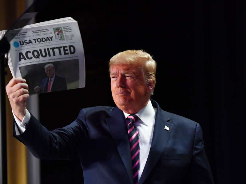 President Donald Trump holds up a newspaper that displays a headline 