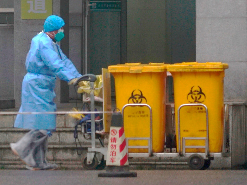 FILE - In this Wednesday, Jan. 22, 2020, file photo, a staff member moves bio-waste containers past the entrance of the Wuhan Medical Treatment Center in Wuhan, China, where some people infected with a new virus are being treated. The new virus comes from a large family of coronaviruses, some causing nothing worse than a cold. Others named SARS and MERS have killed hundreds in separate outbreaks. (AP Photo/Dake Kang, File)