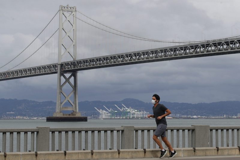 A man wears a mask to protect himself from the coronavirus while running in front of the San Francisco-Oakland Bay Bridge along the Embarcadero in San Francisco, in April.