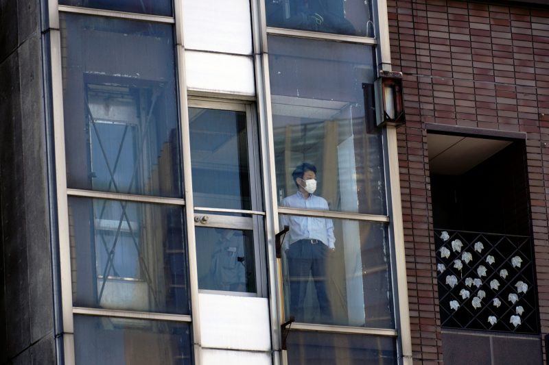 A man wearing a face mask to help curb the spread of the coronavirus stands at a building window in Tokyo Thursday, May 14, 2020. Japan is still under a coronavirus state of emergency which was extended until the end of May though there have been no hard lockdowns. (AP Photo/Eugene Hoshiko)