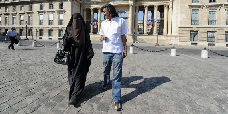 Hind, a Niqab veiled woman (L) and real estate magnate Rachid Nekkaz (R) who supports Muslim women fined for wearing the burka or niqab on the street walk in front of the French National Assembly during a symbolic protest against France's ban on wearing full-face niqab veils in public, on April 20, 2011 in Paris. French officials estimate that only around 2,000 women, from a total Muslim population estimated at between four and six million, wear niqabs, which are traditional in parts of Arabia and South Asia. AFP PHOTO / MEHDI FEDOUACH (Photo credit should read MEHDI FEDOUACH/AFP via Getty Images)