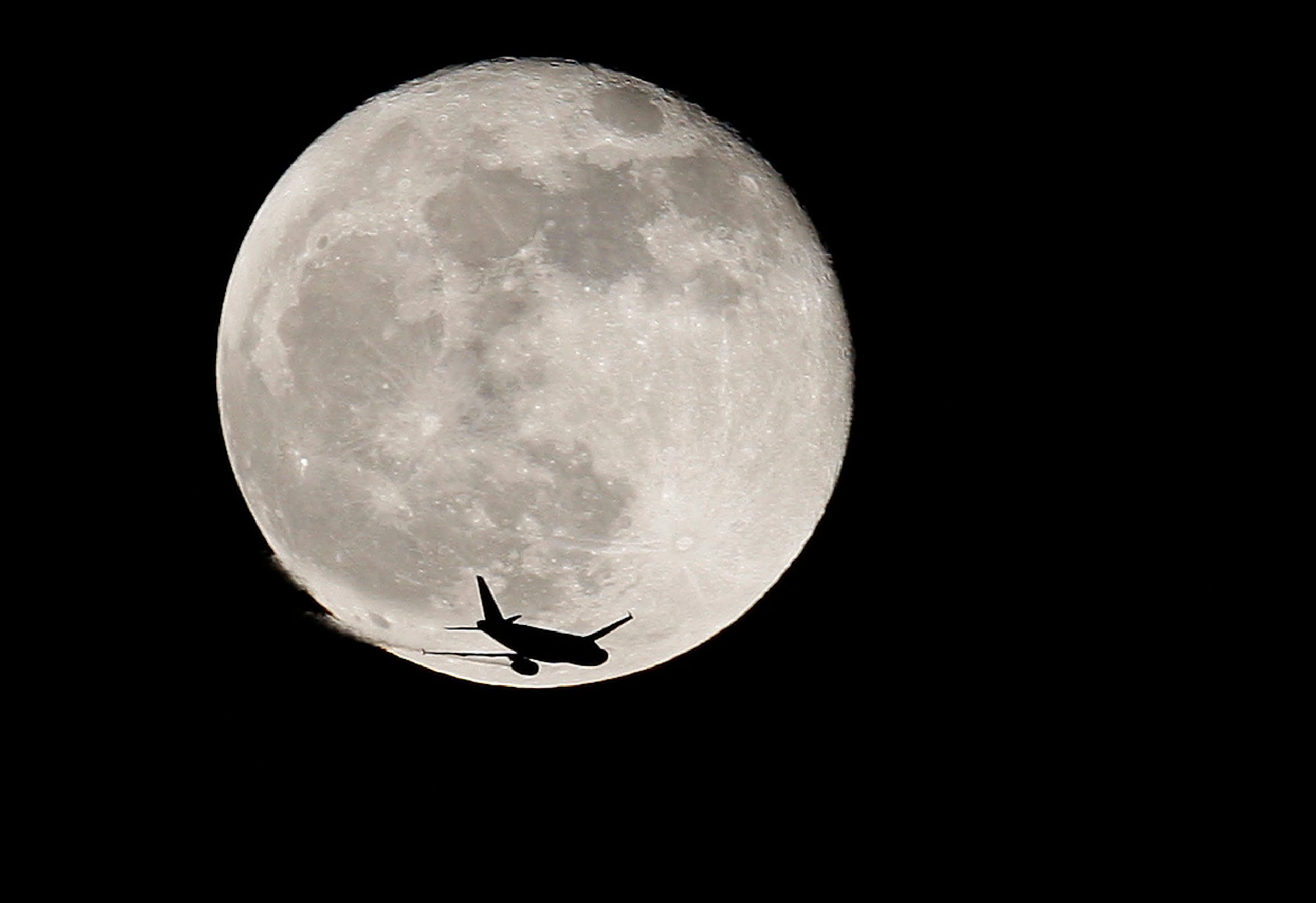 FILE PHOTO: An airplane is silhouetted against a full moon in the sky over London January 1, 2010. REUTERS/Suzanne Plunkett/File Photo