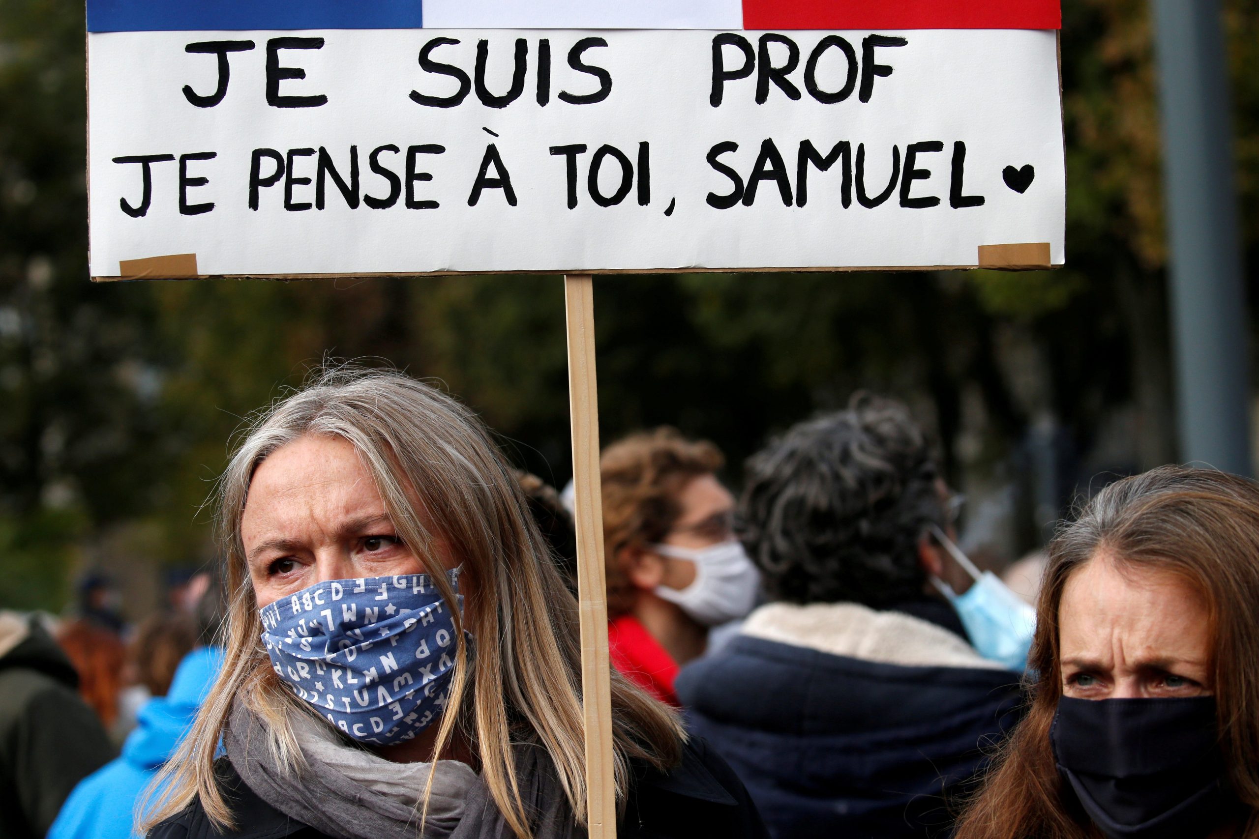 A woman holds a banner as she attends a tribute to Samuel Paty, the French teacher who was beheaded on the streets of the Paris suburb of Conflans St Honorine, at the Place de la Republique, in Lille, France, October 18, 2020.