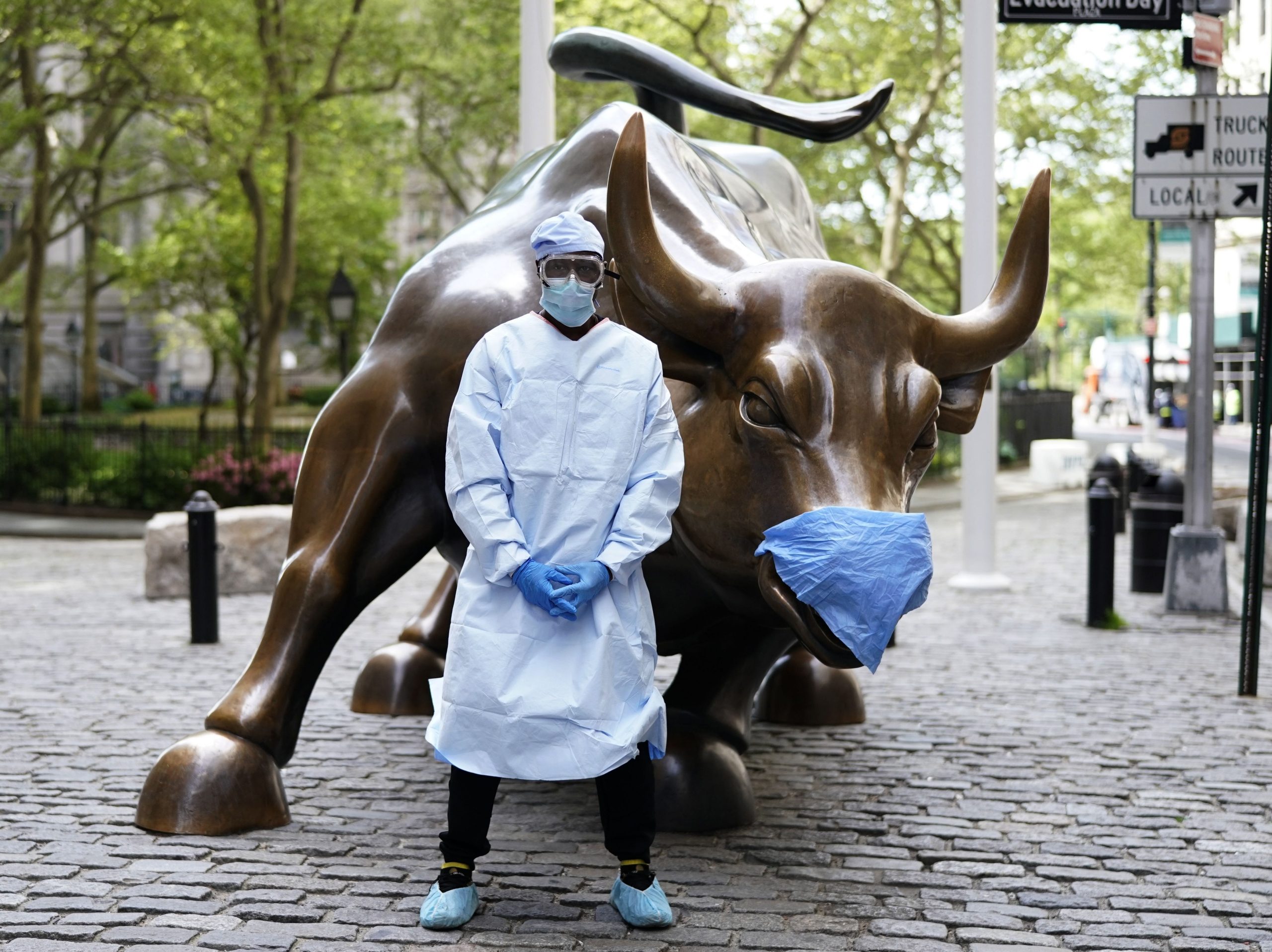 Julius Shakari, from California in full PPE gear, takes photos with his friend in front of the Charging Bull