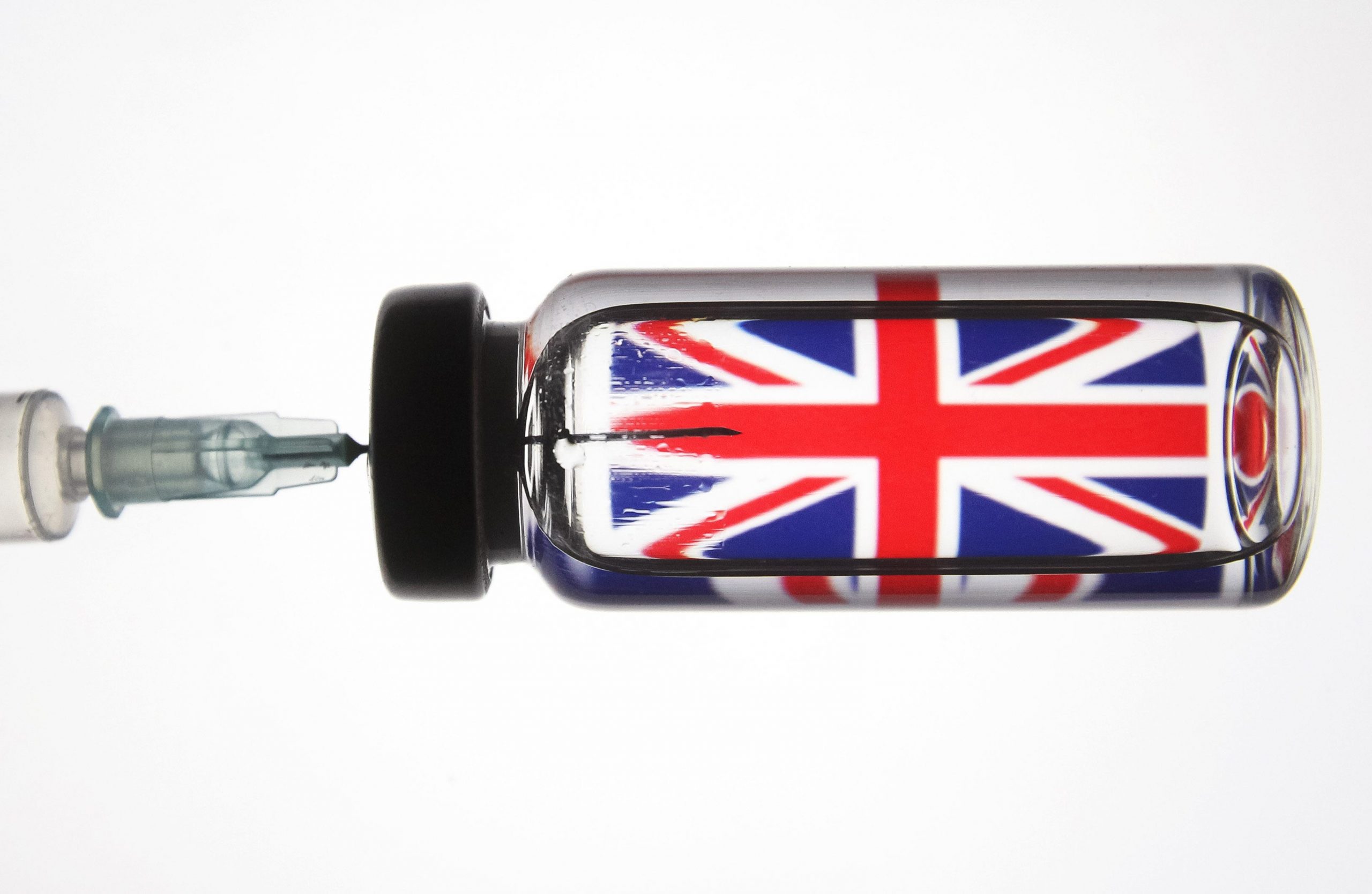 In this photo illustration a medical syringe and a vial depicting fake coronavirus vaccine seen in front of the British flag.