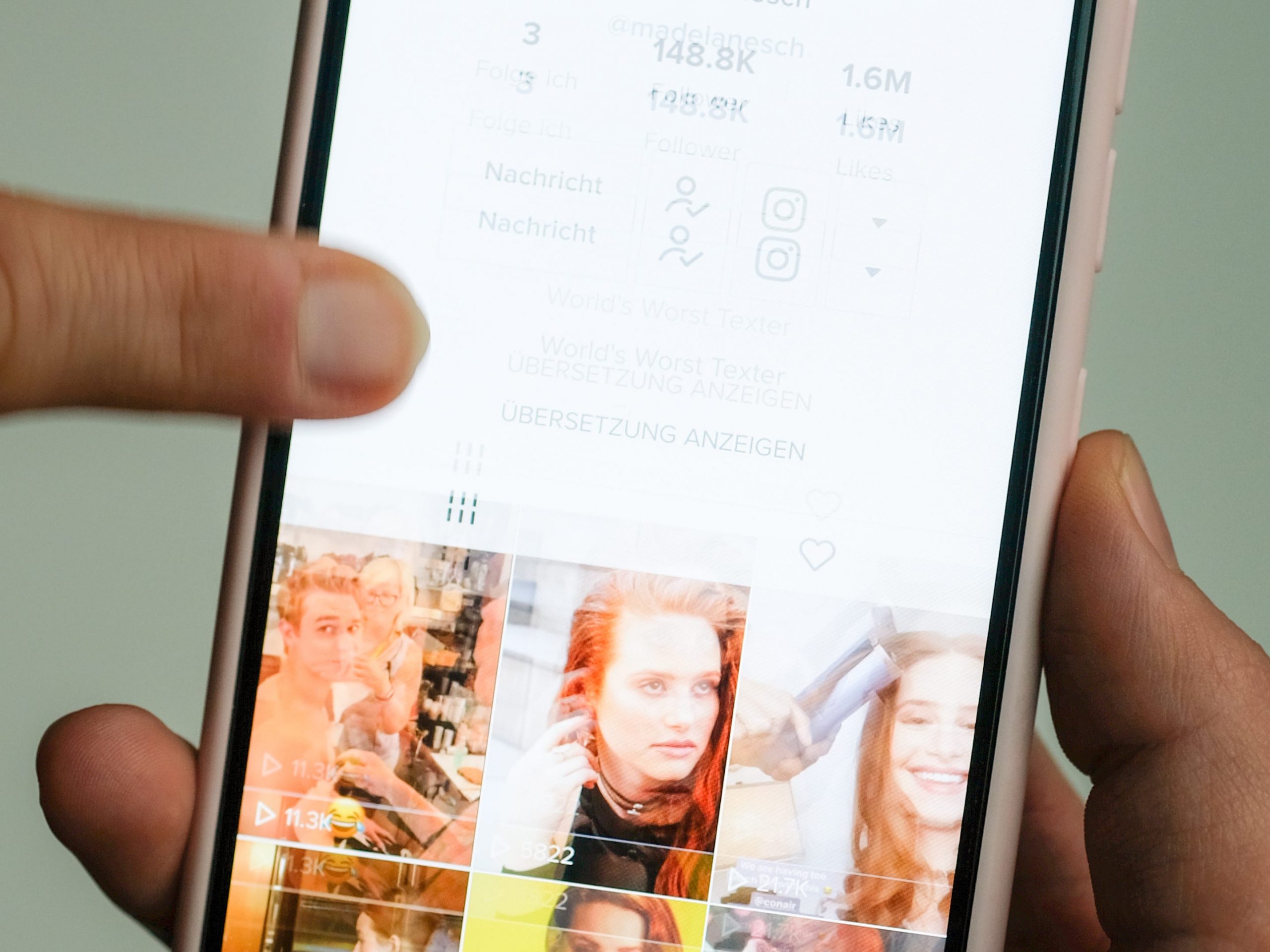 A girl holds her smartphone in her hands on which she has opened @madelainepetsch's profile in the short video app TikTok.