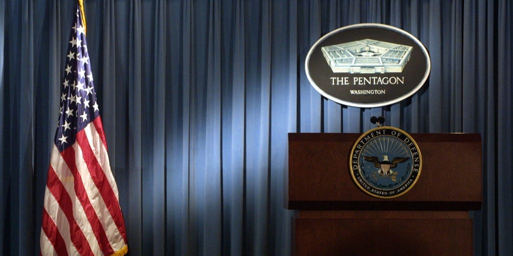 The Pentagon logo and an American flag are lit up January 3, 2002 in the briefing room of Pentagon in Arlington, VA